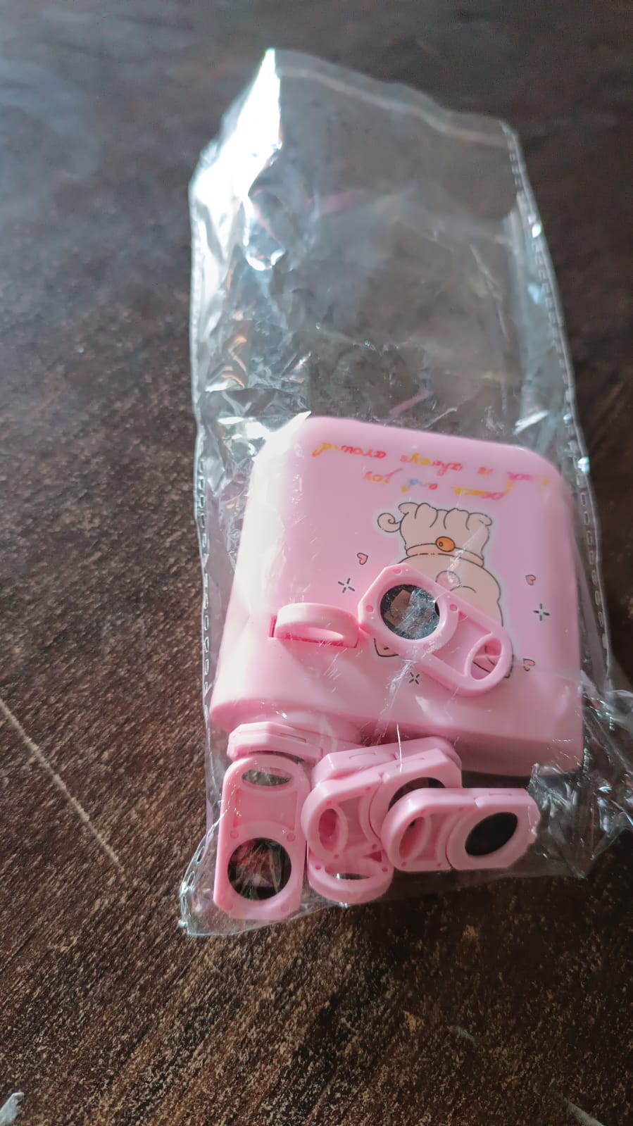 The pink puppy projector and its slide cartridges are sealed in clear plastic packaging on a wooden surface.