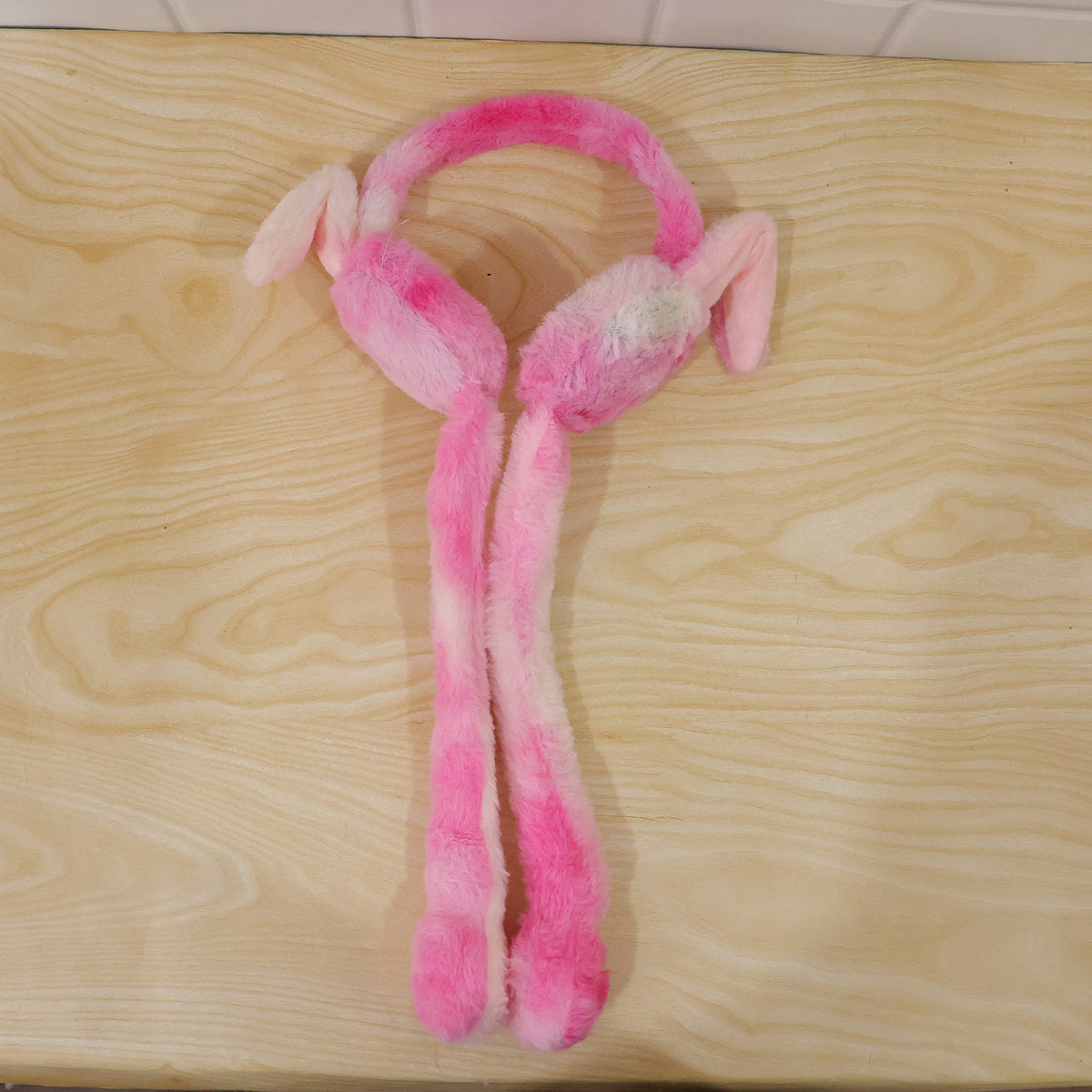 Pink and white plush bunny earmuffs with long tails lying on a light wooden surface.