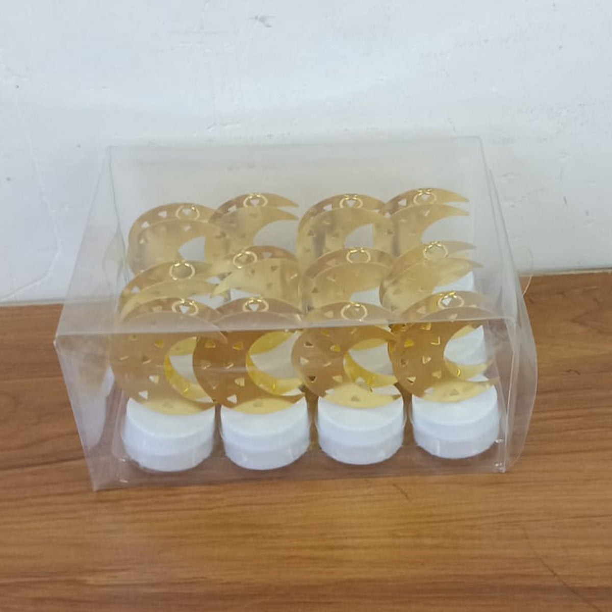 Twelve gold moon shaped flameless LED candles packaged in a clear plastic box on a wooden surface.