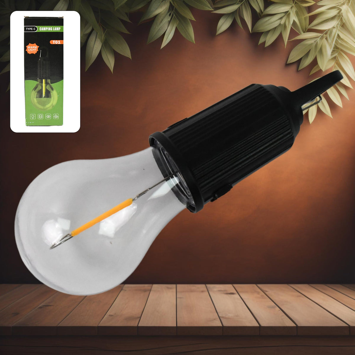 A clear LED bulb with a black top and hook is on a wooden surface, with its green and black packaging in the top left.