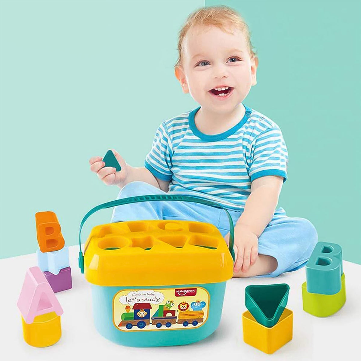 A smiling baby sits behind a blue and yellow shape sorter bucket with various colorful blocks around it on a light blue