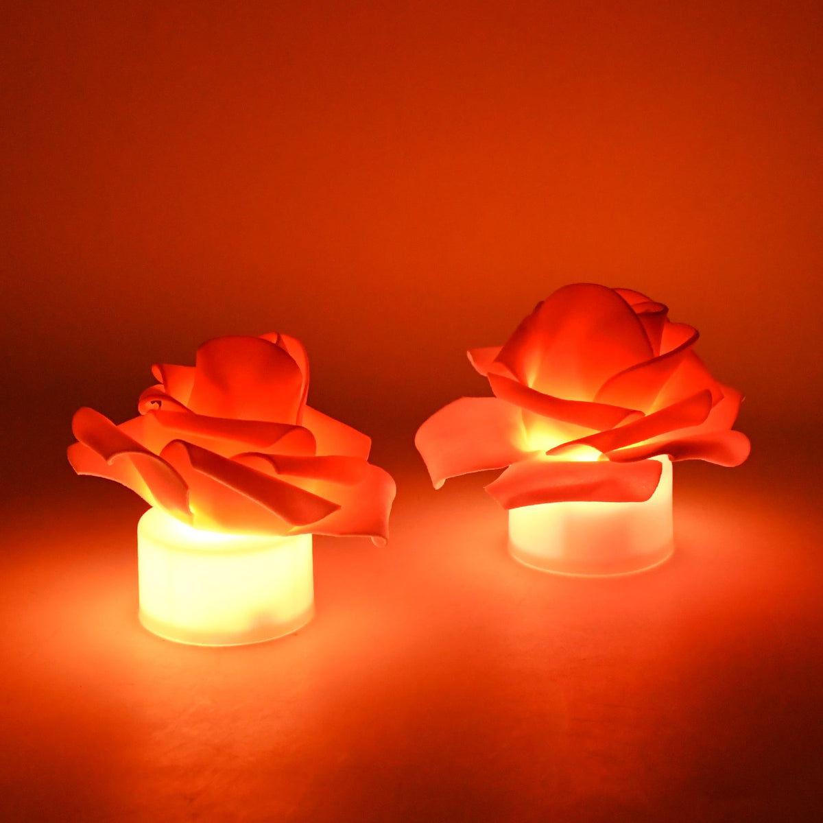 Two glowing orange LED rose tea lights on a dark orange background, emitting a warm light.