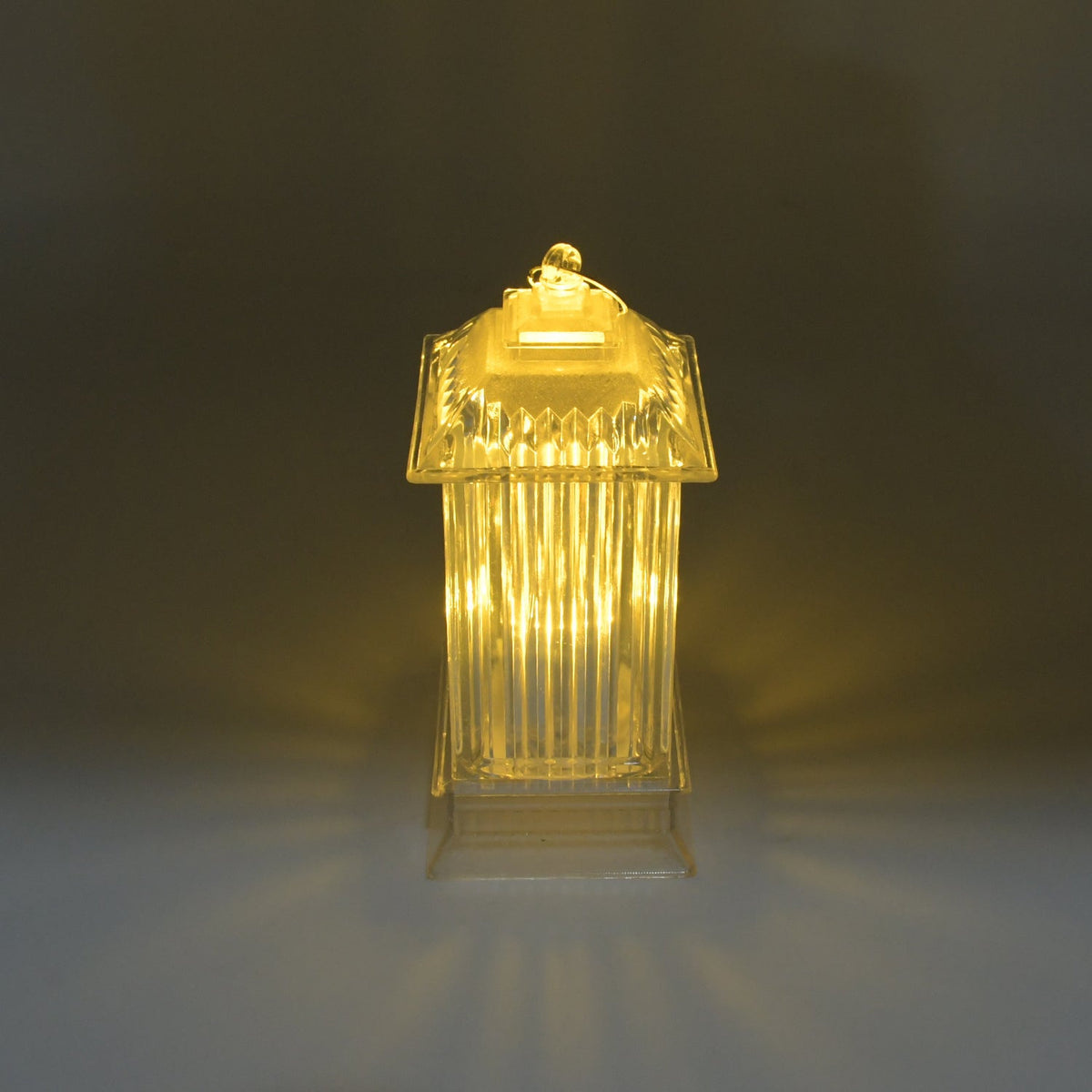 A single LED crystal lantern lamp emits a soft, warm glow on a subtly reflective surface in a dimly lit setting.