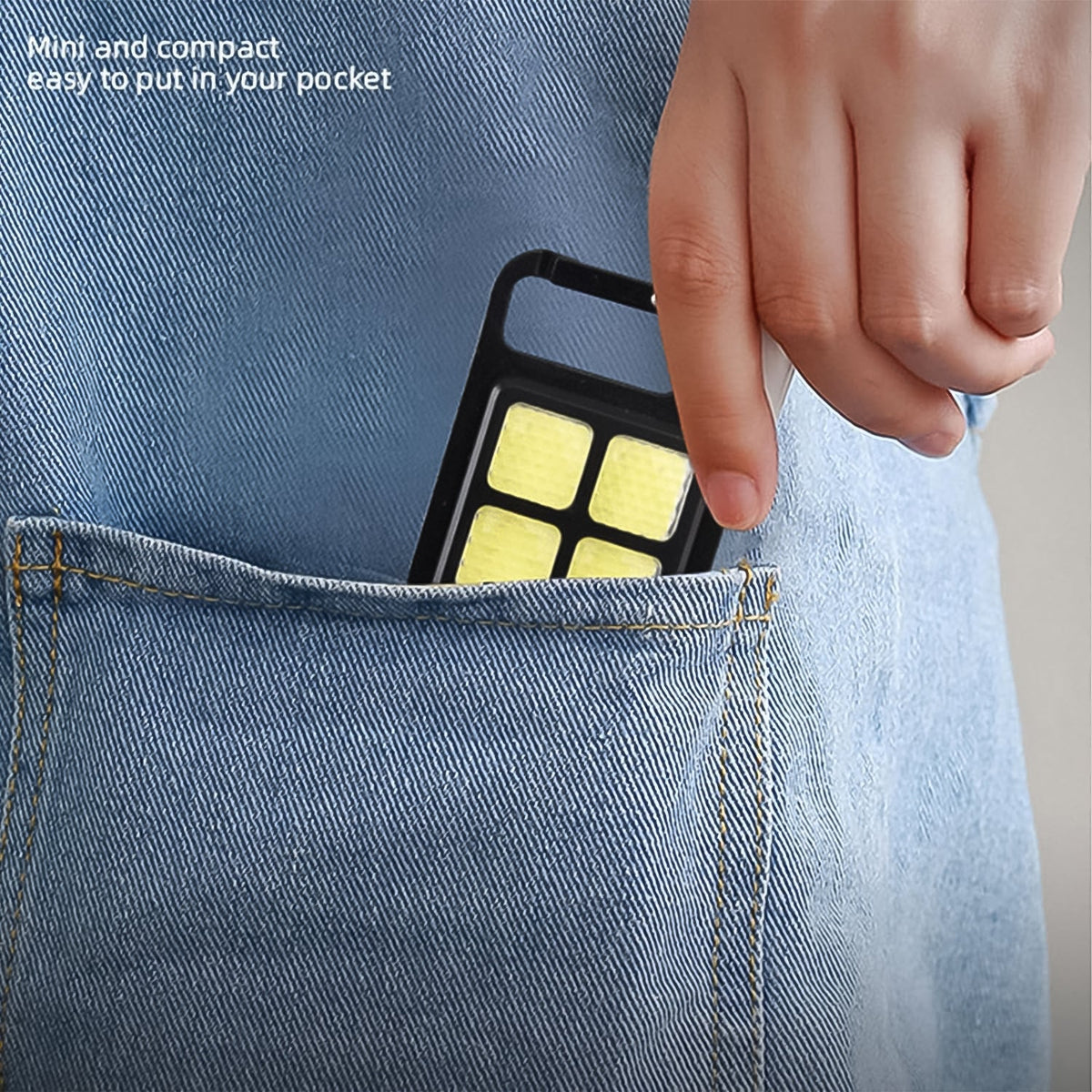 A hand placing the black mini LED keychain light into the back pocket of blue jeans, highlighting its compact size.