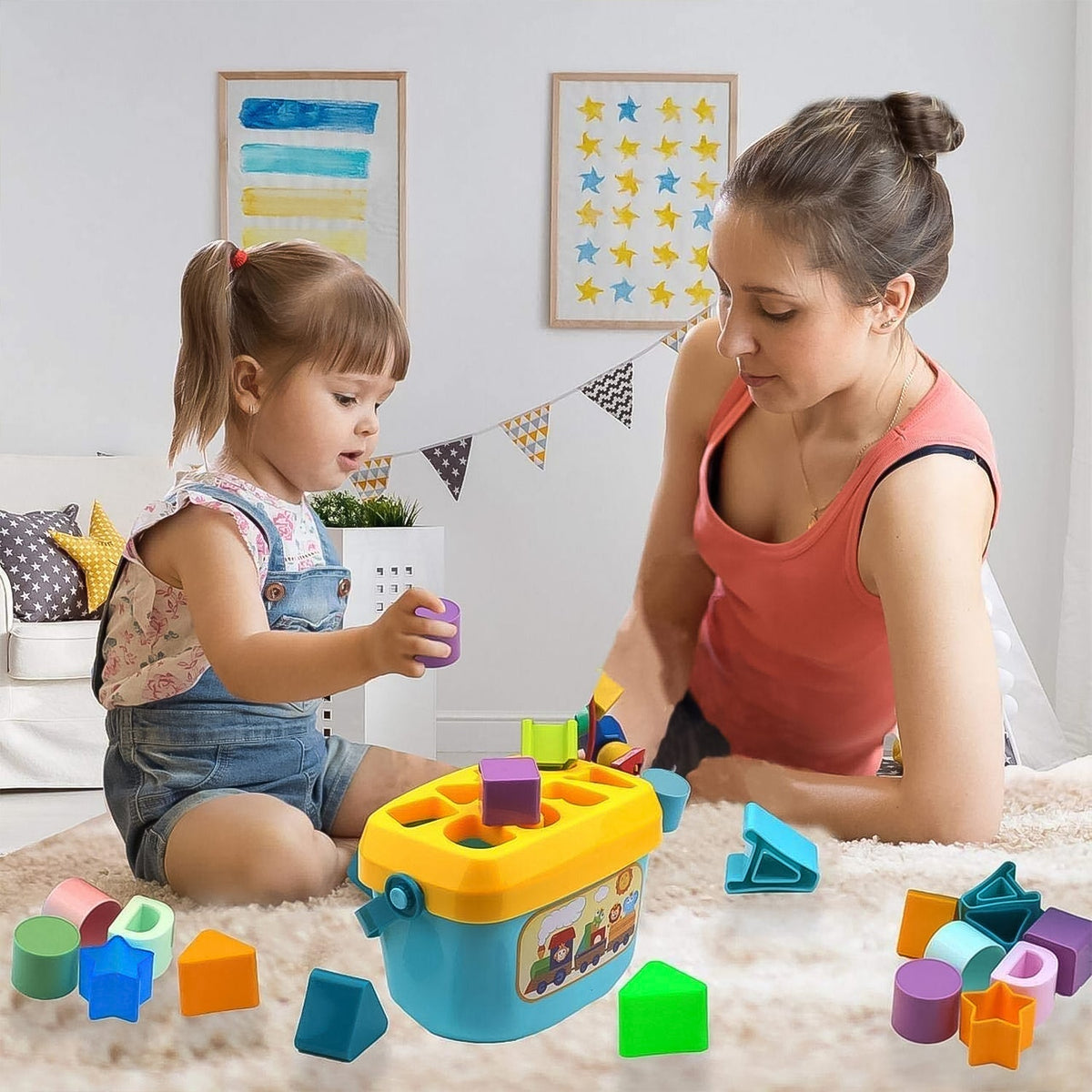 A young girl and an adult play with a blue and yellow shape sorter bucket and colorful blocks on a light-colored rug.