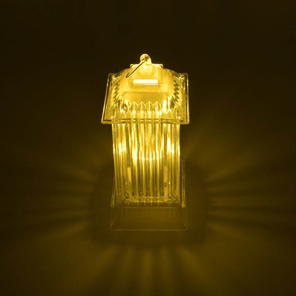 A single LED crystal lantern lamp glows with warm light, casting radial patterns on a dark, reflective surface.