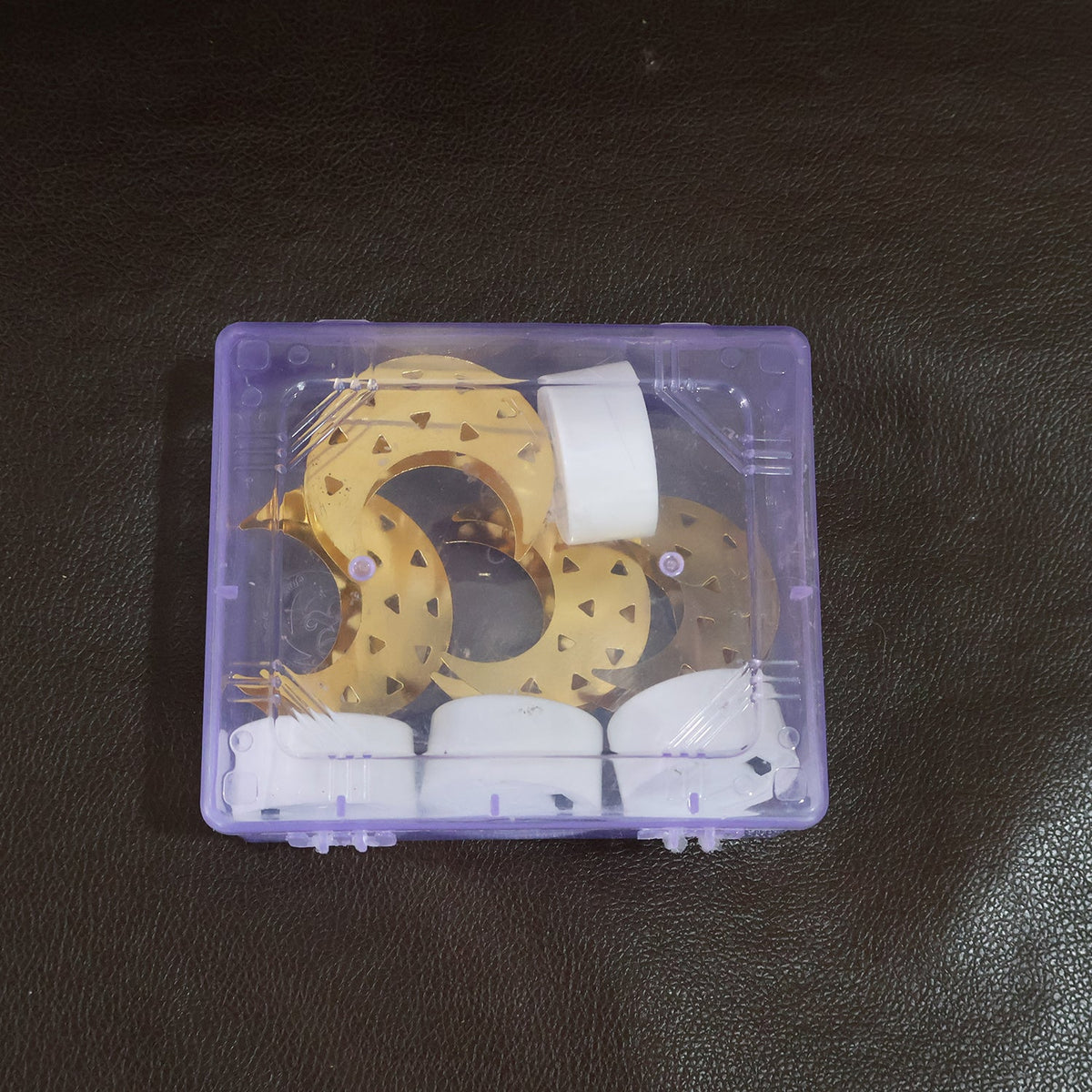 A clear plastic box containing four disassembled crescent moon LED tea lights, with gold moon shapes and white bases.