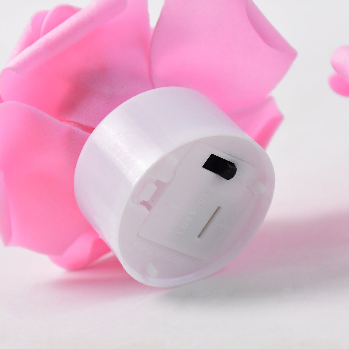 Close-up of the bottom of a white tea light base with a black on/off switch, surrounded by pink rose petals.