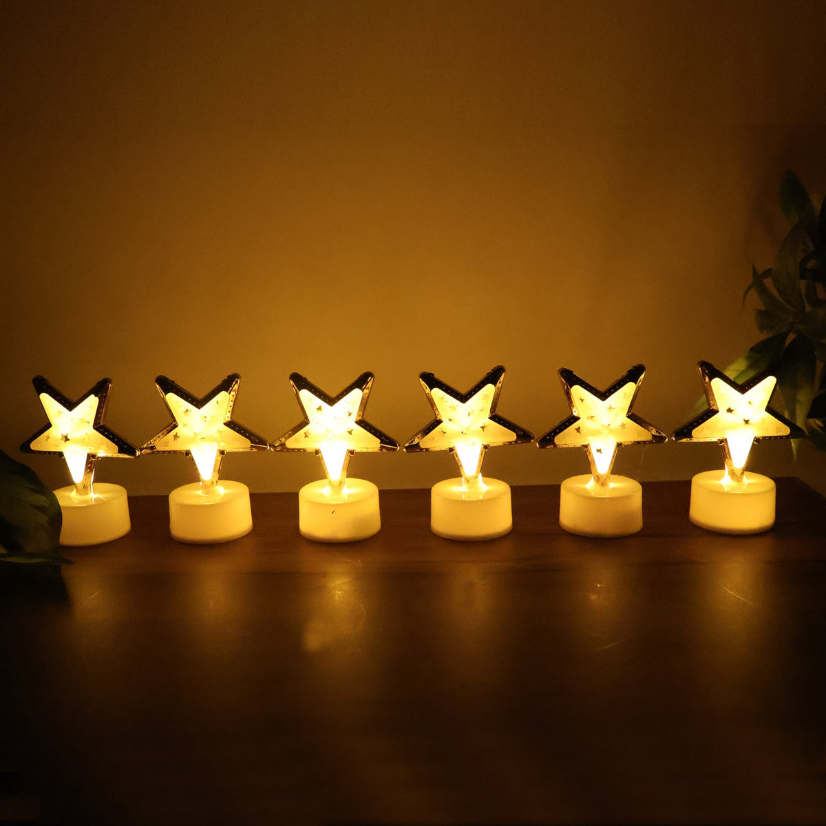 Six glowing star-shaped LED candles with gold frames and white bases lined up on a dark wooden surface.