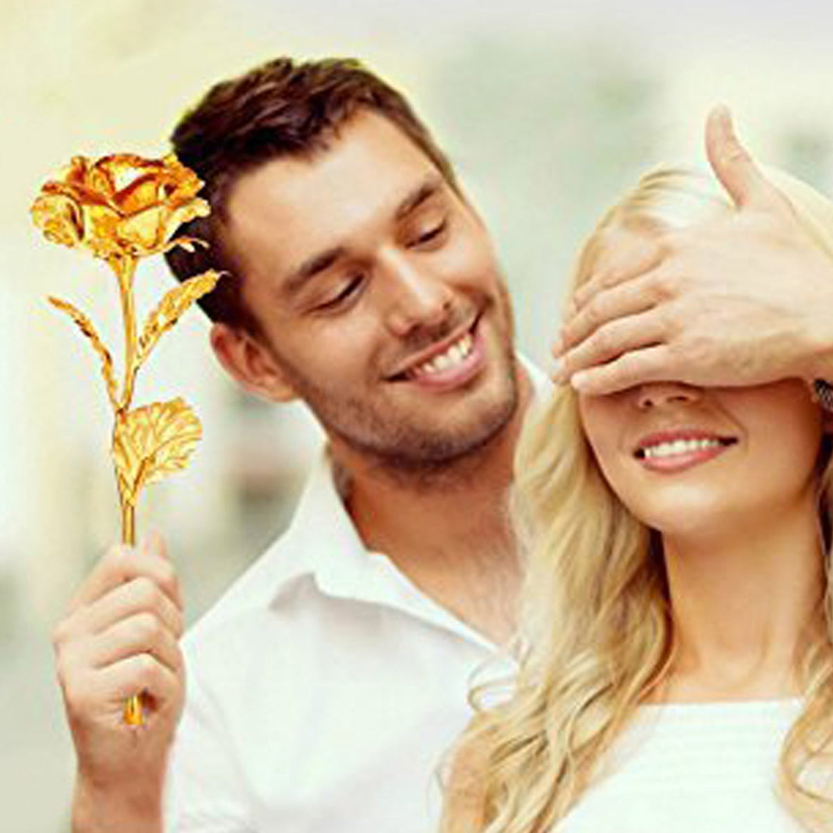 A man with a beard smiles while covering a woman's eyes, holding a gold-plated rose in his hand.