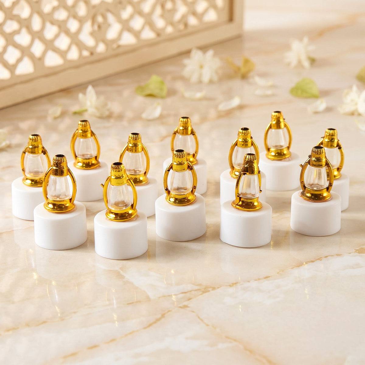 A dozen small golden lantern LED candles are neatly arranged on a light marble surface with delicate white floral petals