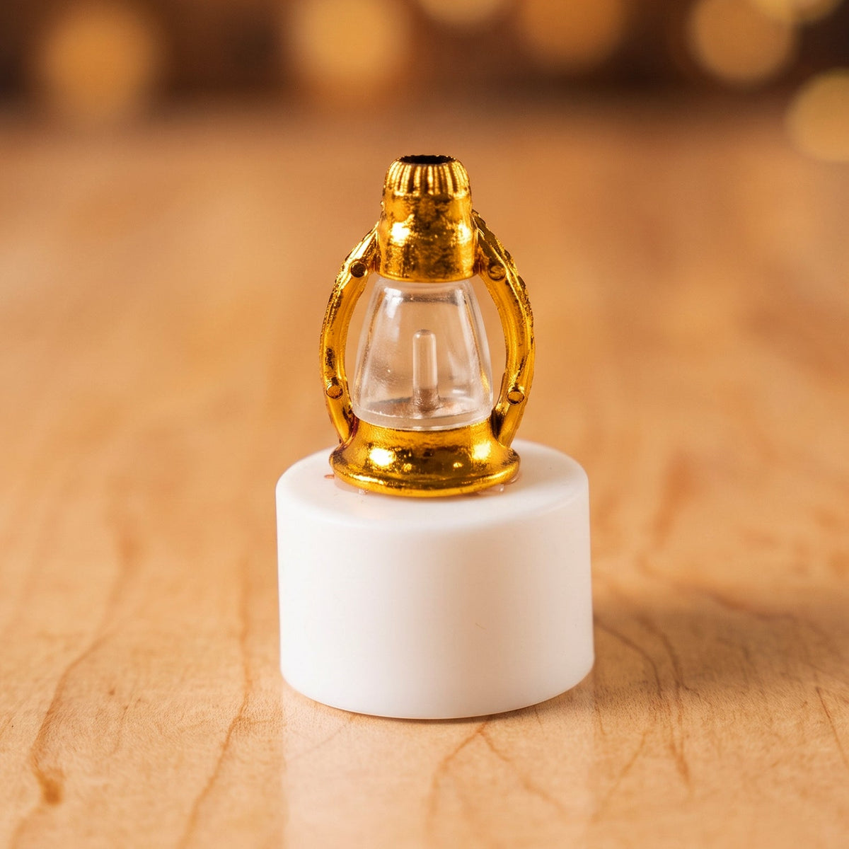 A single miniature golden lantern LED candle with a clear glass body sits on a wooden surface, glowing softly.