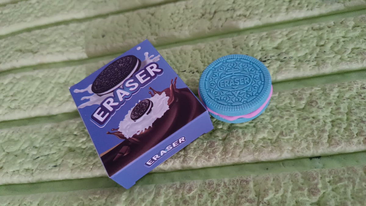 A blue and pink cookie-shaped eraser and its packaging box are placed on a textured green surface.