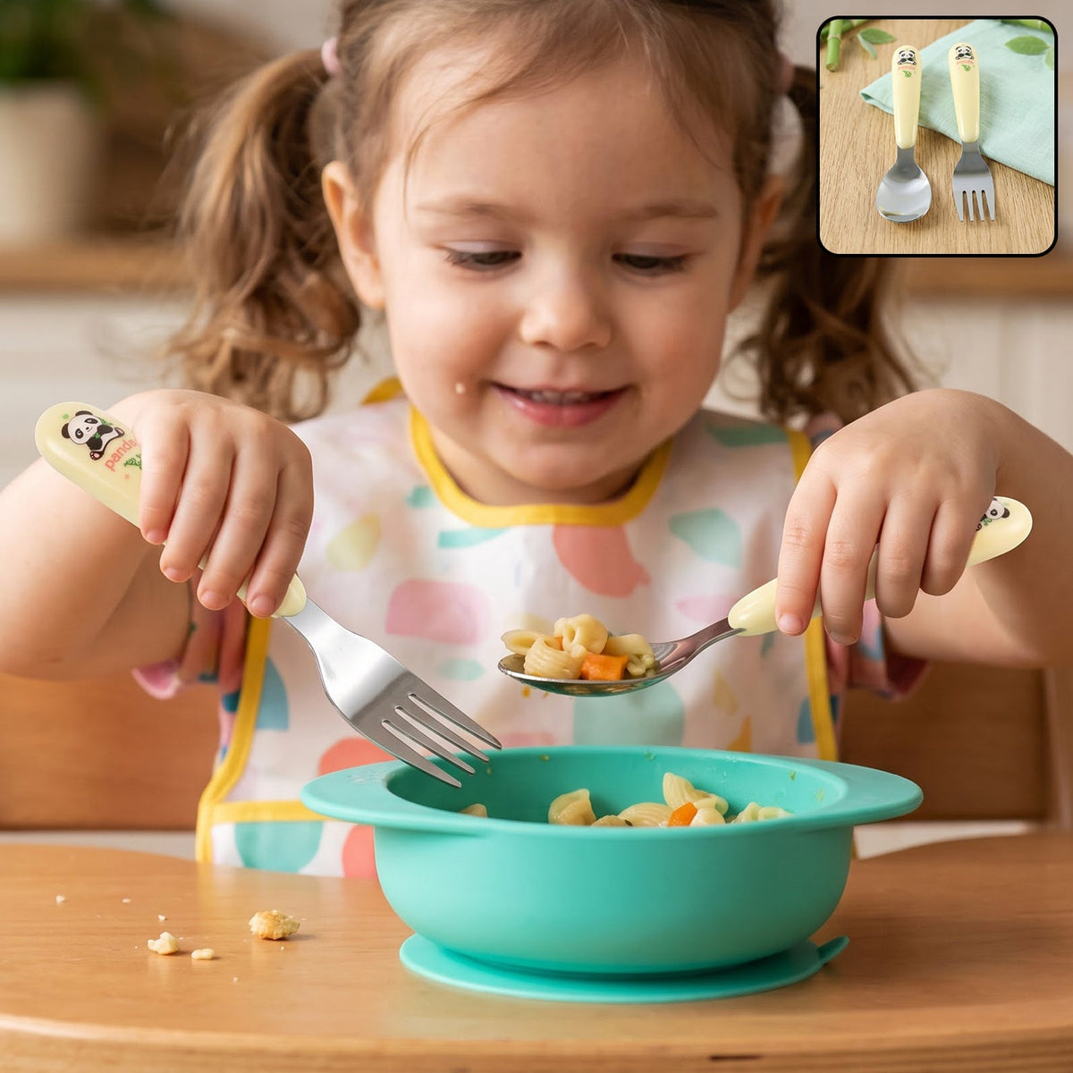 A young girl in a bib holds a panda-handled fork and spoon, eating pasta from a teal bowl.