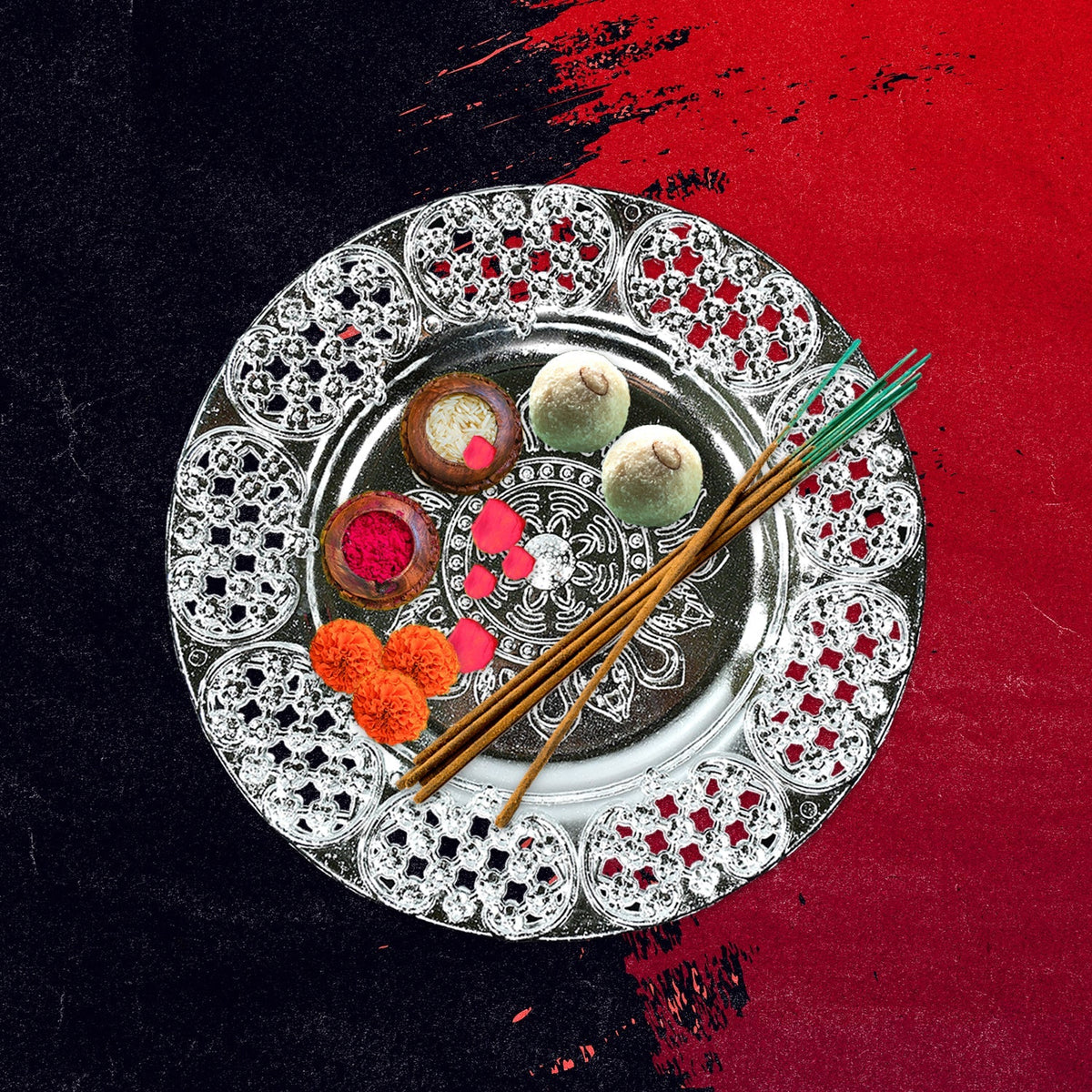 A silver-colored plastic pooja thali filled with sweets, incense sticks, and flower petals on a red and black textured