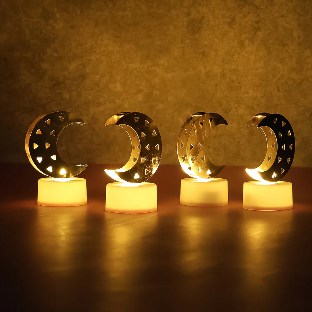 Four crescent moon LED tea lights with warm yellow glow on a reflective wooden surface, creating a cozy ambiance.