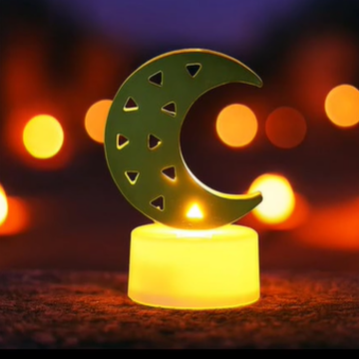 A single crescent moon LED tea light with a warm yellow glow, surrounded by blurred orange lights in the background.