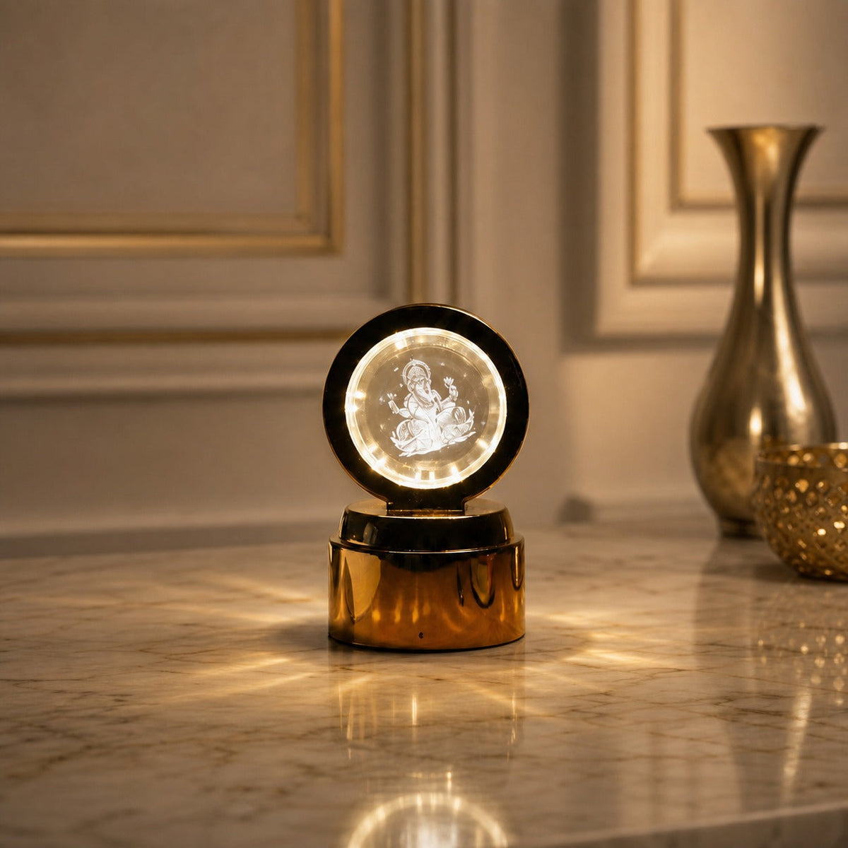 A golden base lamp with a round crystal displaying a glowing Ganesha, on a marble table with a golden vase.