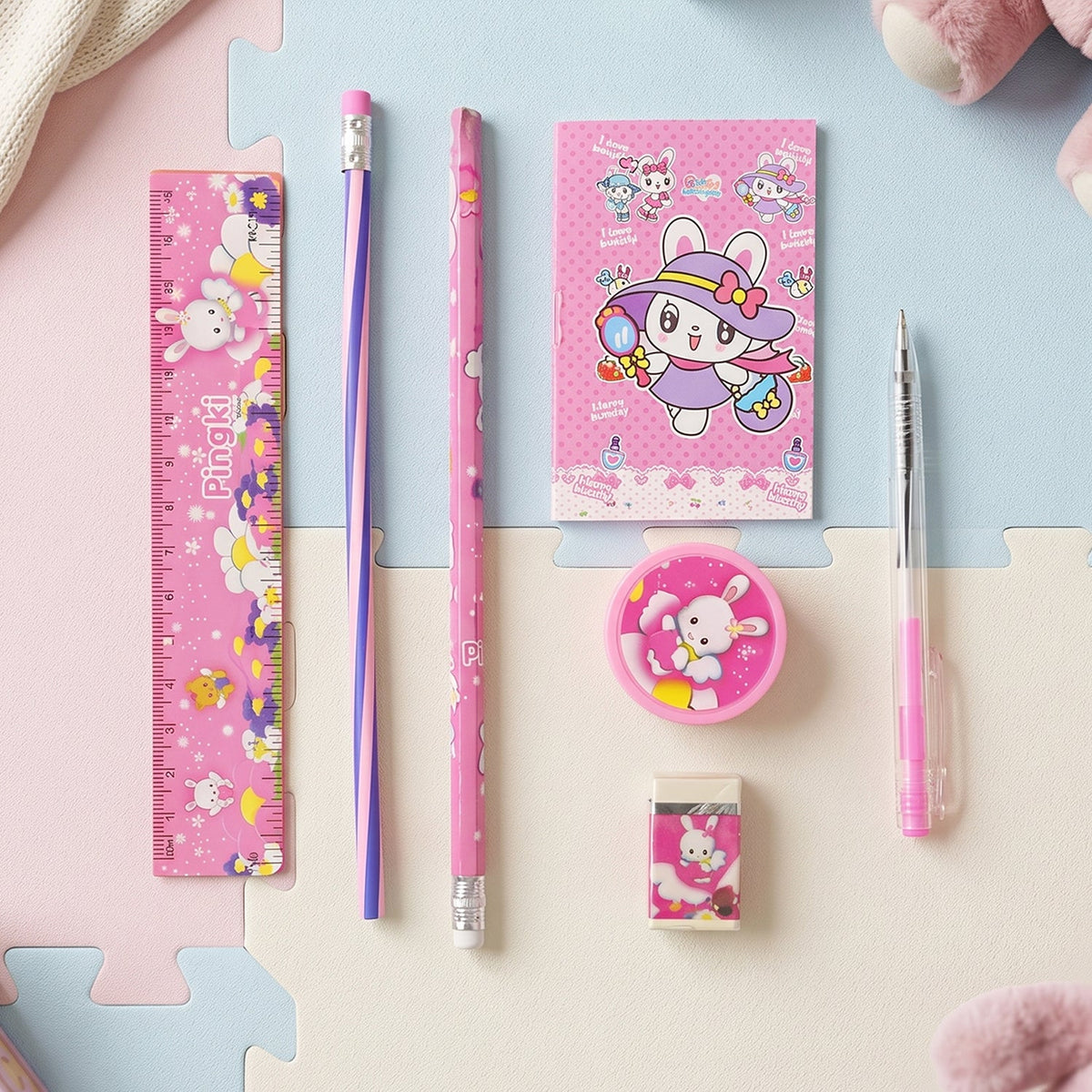 A pink rabbit-themed stationery set arranged neatly on a light blue and pink foam mat, viewed from above.