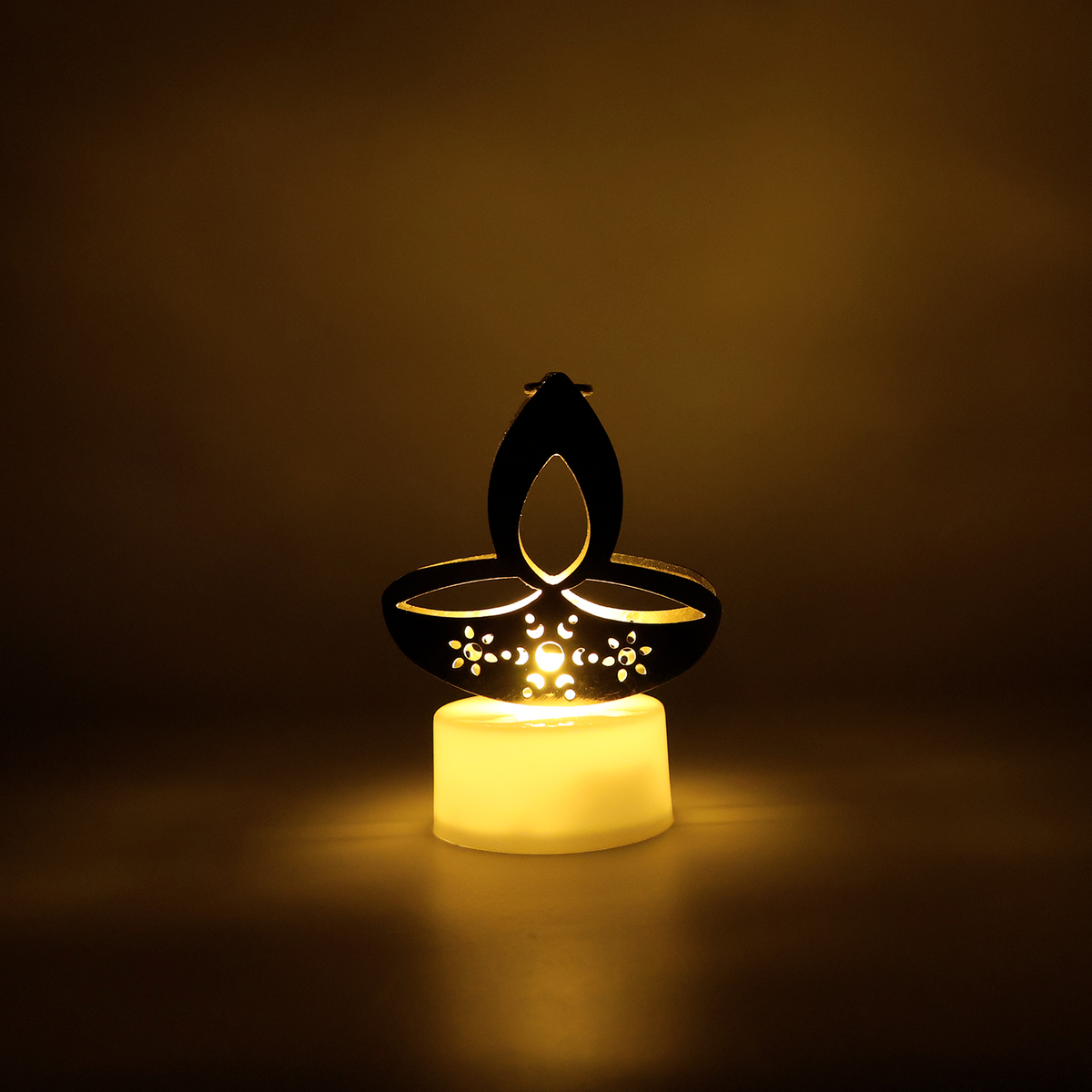 A single golden LED diya tealight candle glowing brightly in a dark, warm-toned setting.