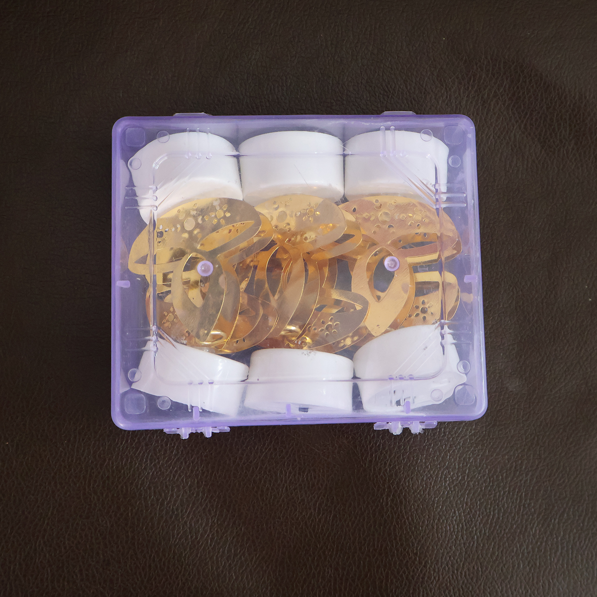 Six golden LED diya tealight candles with white bases packed neatly inside a clear purple plastic storage box.