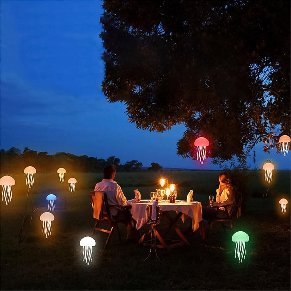 A couple dines outdoors at dusk, surrounded by multiple glowing jellyfish lamps in various colors on the ground and hanging