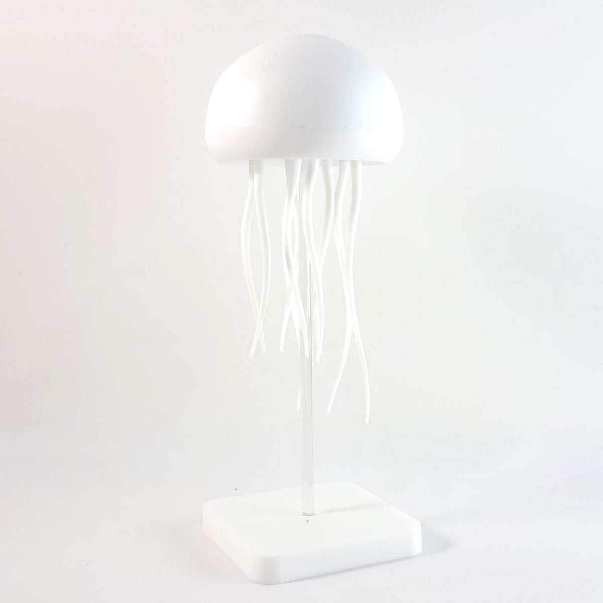 A white jellyfish lamp with a clear stand and square base, presented against a plain white background.