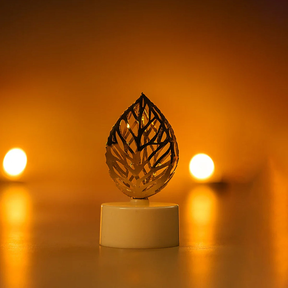 A single golden leaf LED candle glows brightly in a close-up shot against a blurred, warm-toned background.
