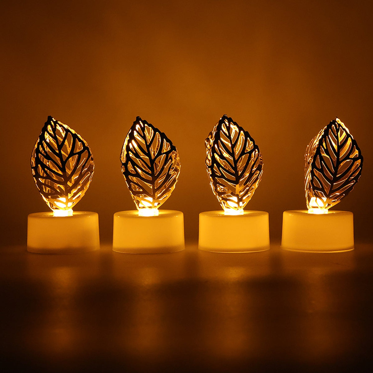 Four golden leaf LED candles emit a warm glow in a dark setting, arranged in a line.