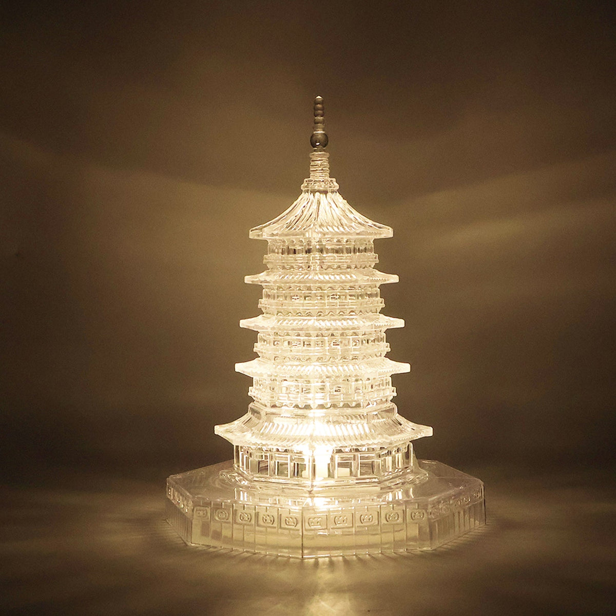 A clear, illuminated LED crystal pagoda light casting a warm glow on a dark, textured background.