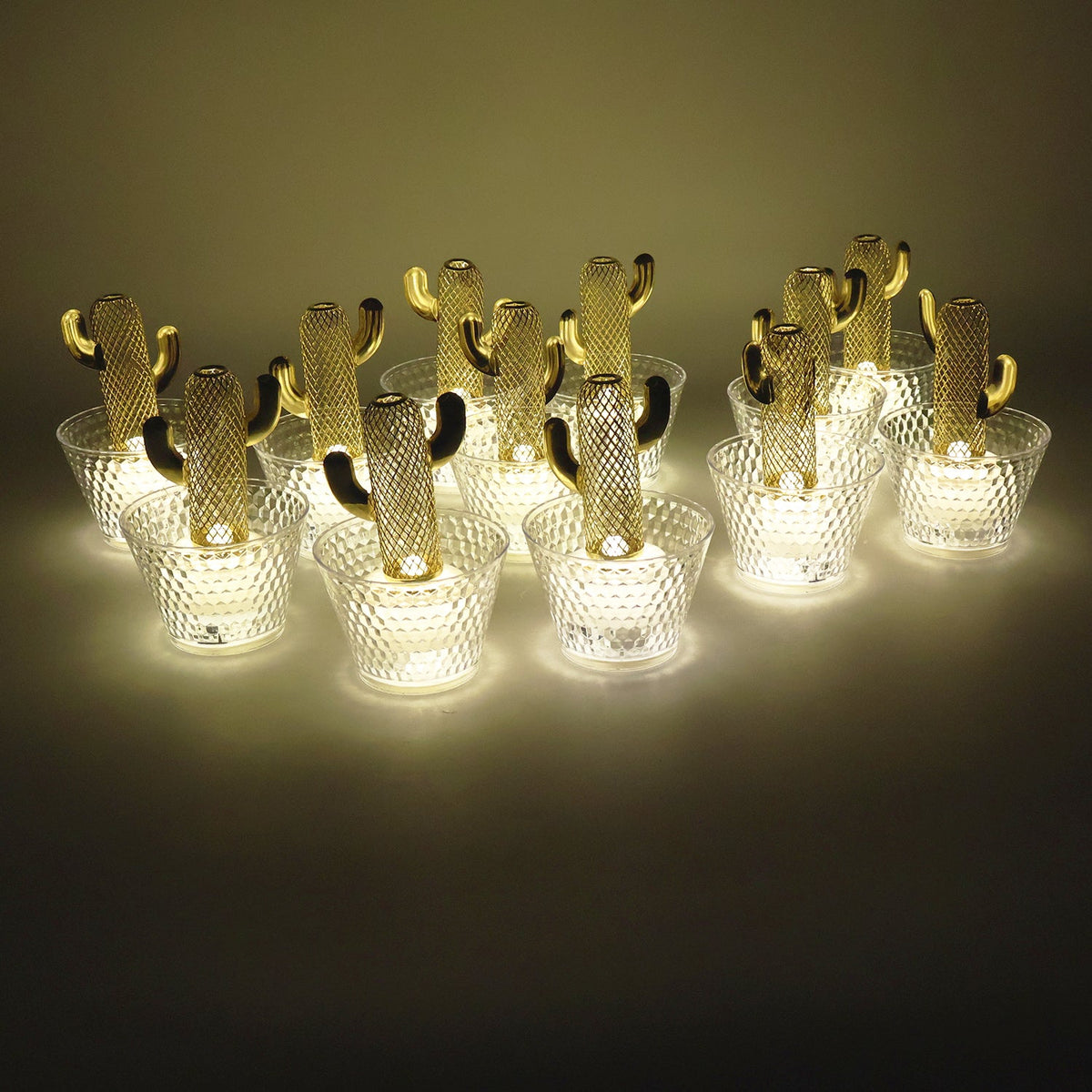 Twelve gold cactus LED tealights with clear textured bases emit a warm glow in a dimly lit setting.