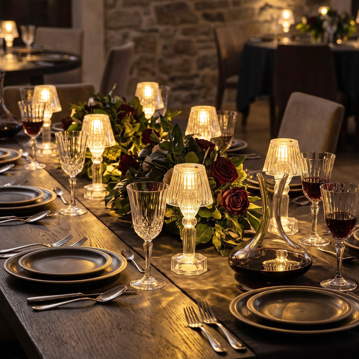 An elegant dining table features multiple illuminated clear acrylic LED lamps, with wine glasses and a dark floral