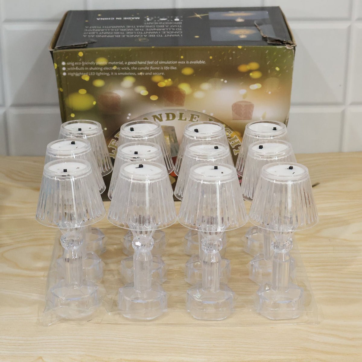 Ten clear acrylic miniature lamps are packaged in a clear plastic tray, positioned in front of a brown cardboard box.