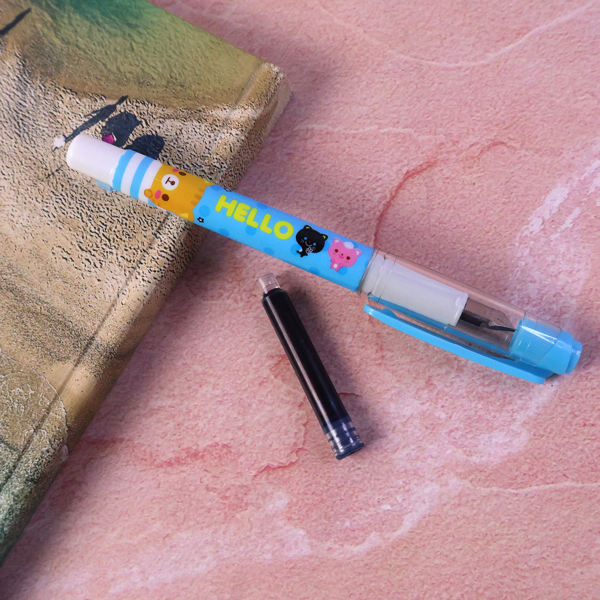 A light blue cartoon animal fountain pen with one black ink cartridge on a pink and brown surface.