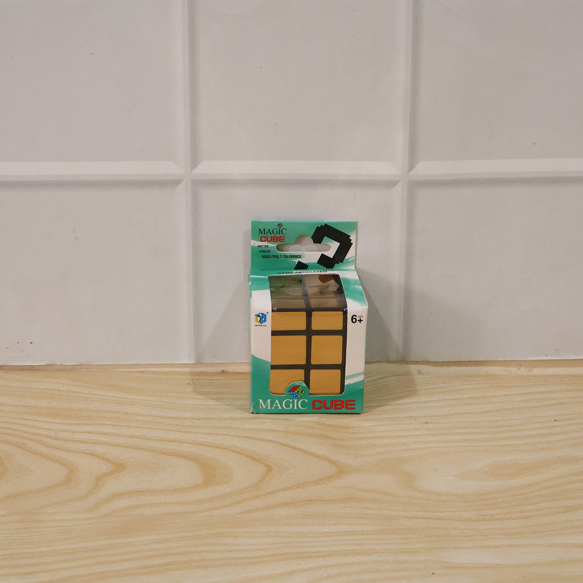 A small green and white package for a "Magic Cube" with a gold mirror cube pictured on it, sits on a wooden surface against