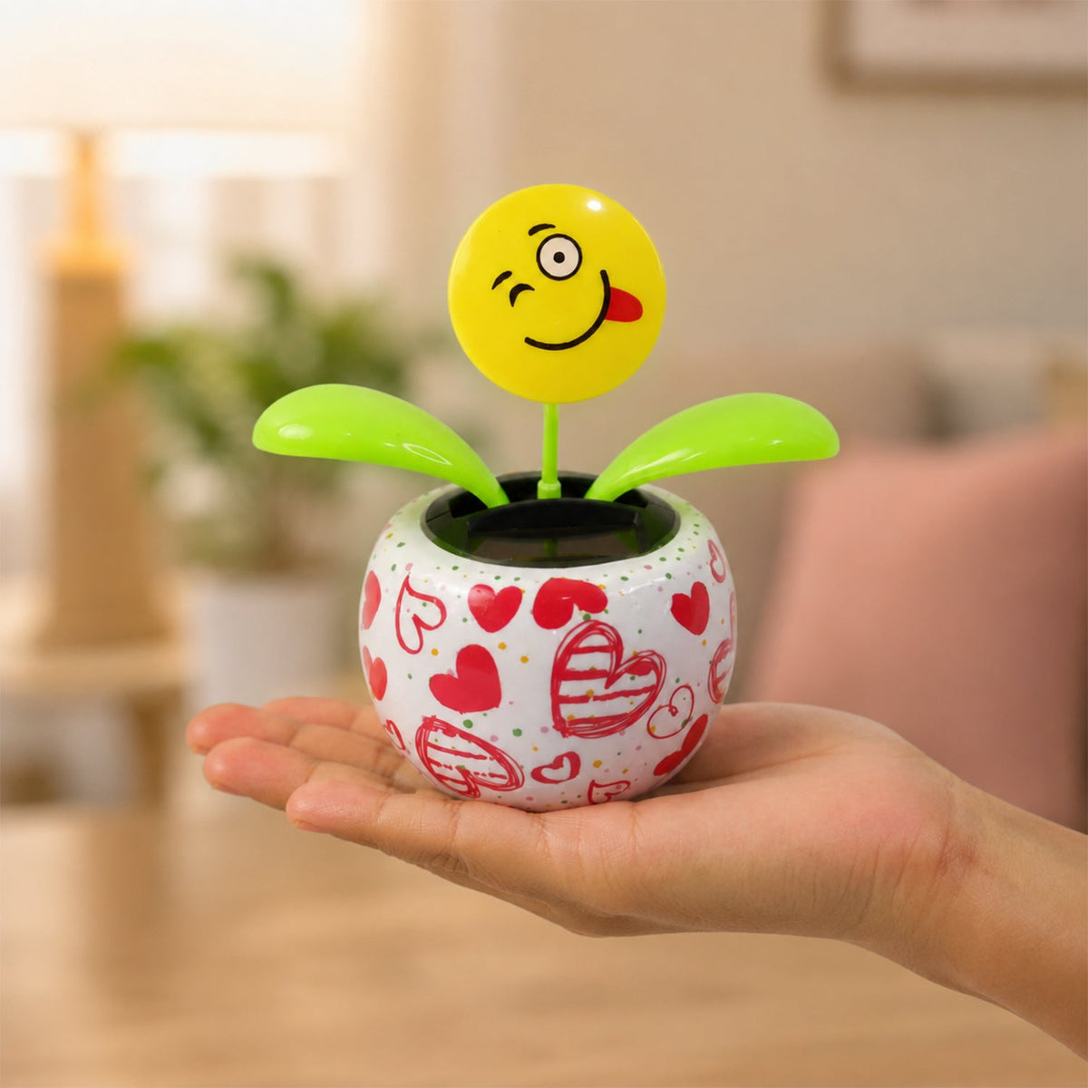 A person's hand holding a white pot with red hearts, containing a winking emoji face solar dancing flower.