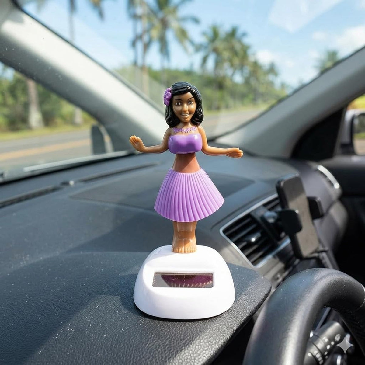 A solar-powered dancing hula girl toy in purple and brown, with a white base, on a car dashboard with palm trees visible.