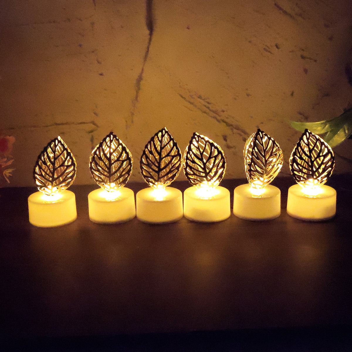 Six golden leaf LED candles glowing in a row on a dark surface against a textured background.