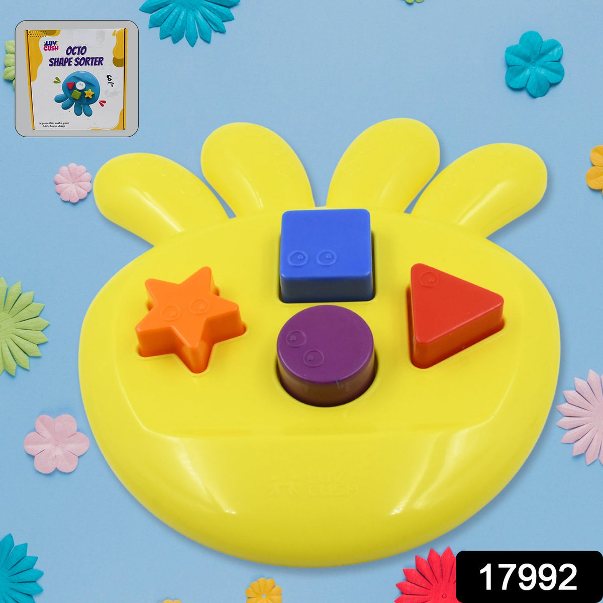 Yellow shape sorter with colorful blocks on a blue background surrounded by small decorative flowers and a product label.