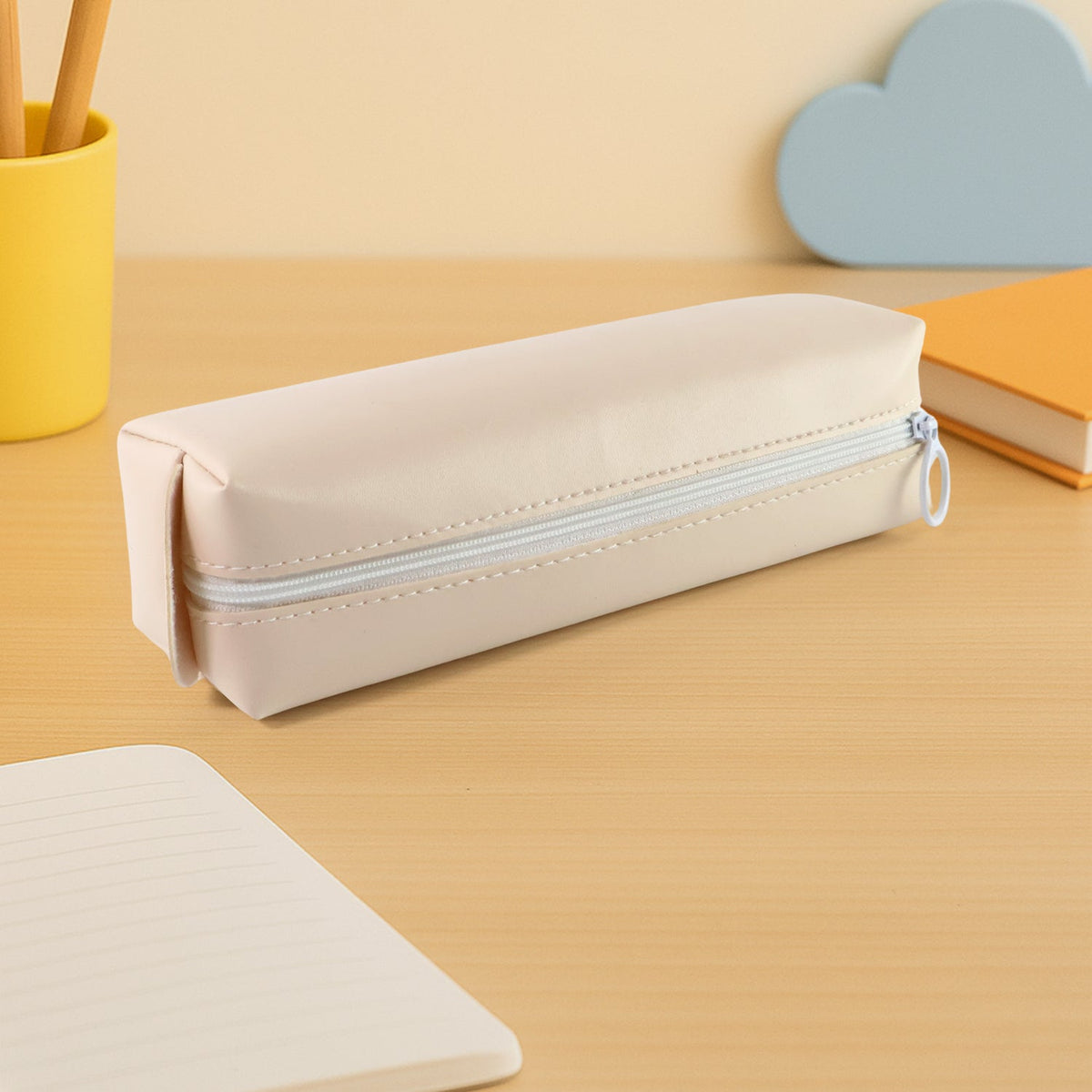 Closed beige pencil case on a light wooden desk with a yellow pen holder and blue cloud decor.